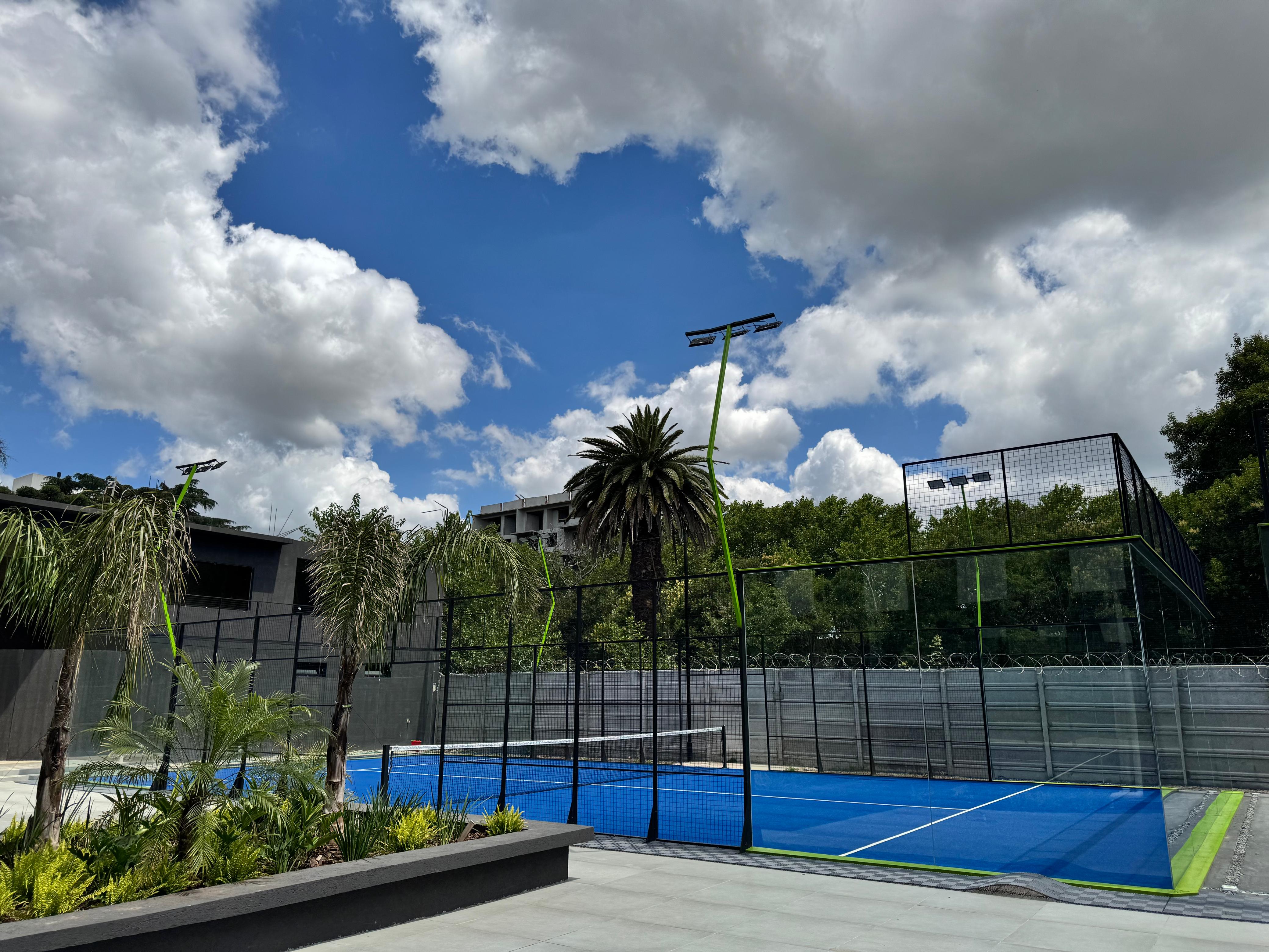 Cancha de pádel modelo premium Blue Court con superficie azul, paisajismo tropical y estructura moderna